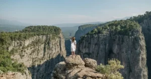 Woman standing on cliff overlooking mountainous landscape.