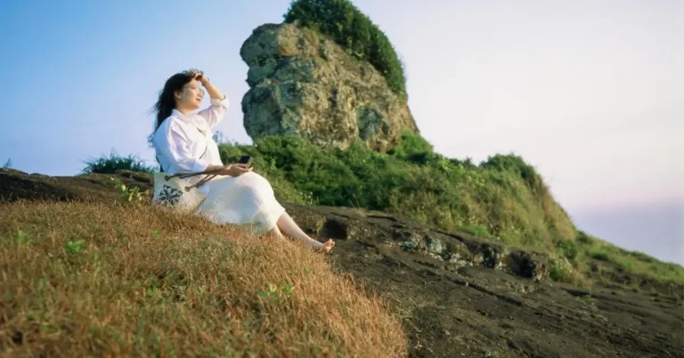 Person relaxing on a hillside by rocky landscape.