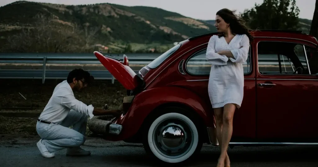 Man fixing red car, woman standing nearby.
